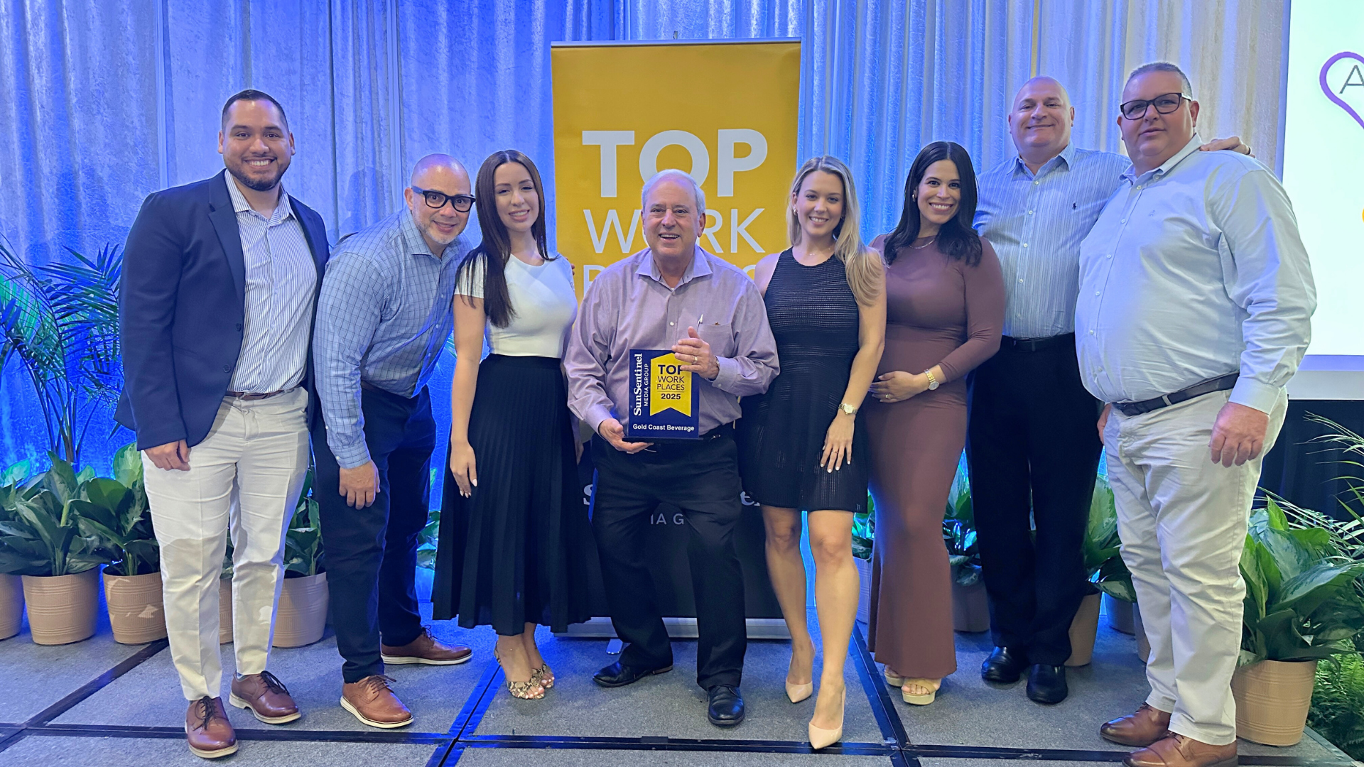 Group of people smiling in front of a workplace award backdrop