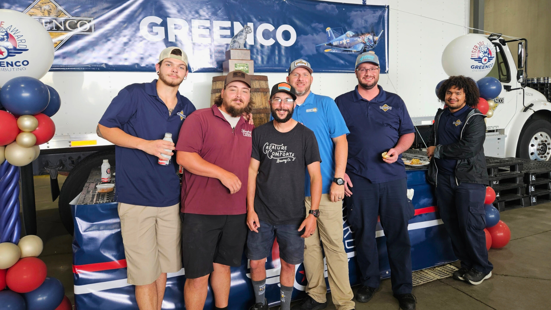 Six people smiling in front of a parked delivery truck with a banner that says Greenco
