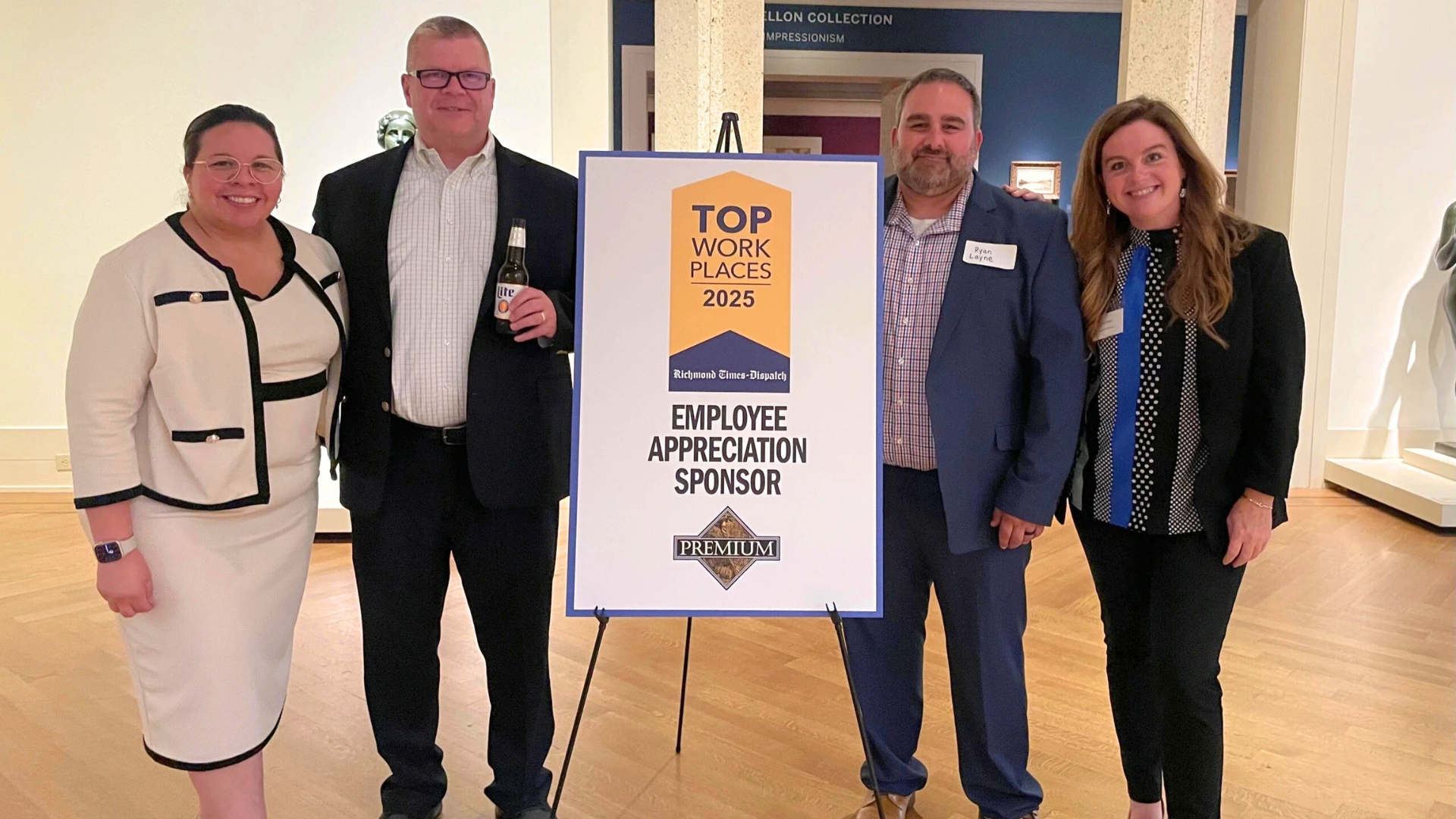 Four people smiling while standing next to a Top Workplaces award sign