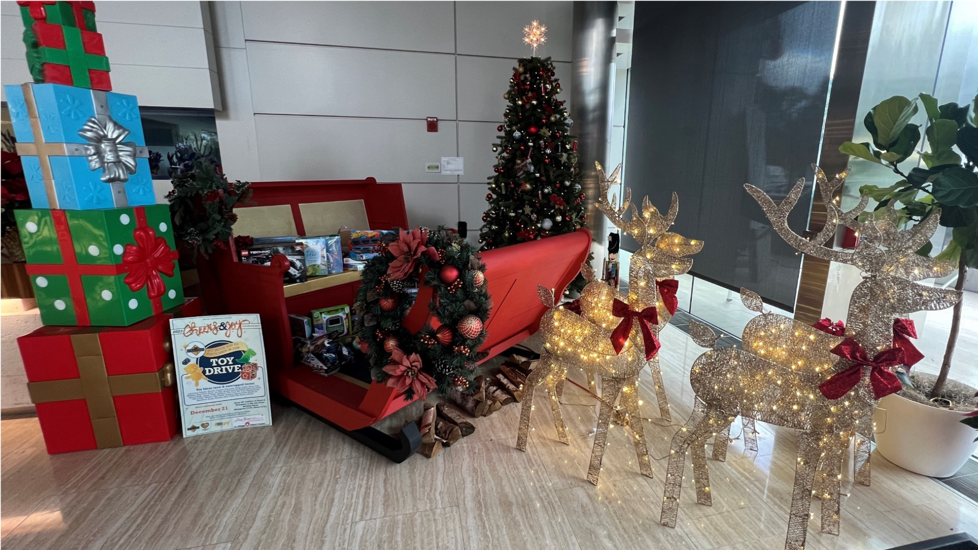 toys in a red sleigh next to a toy drive sign and christmas decorations