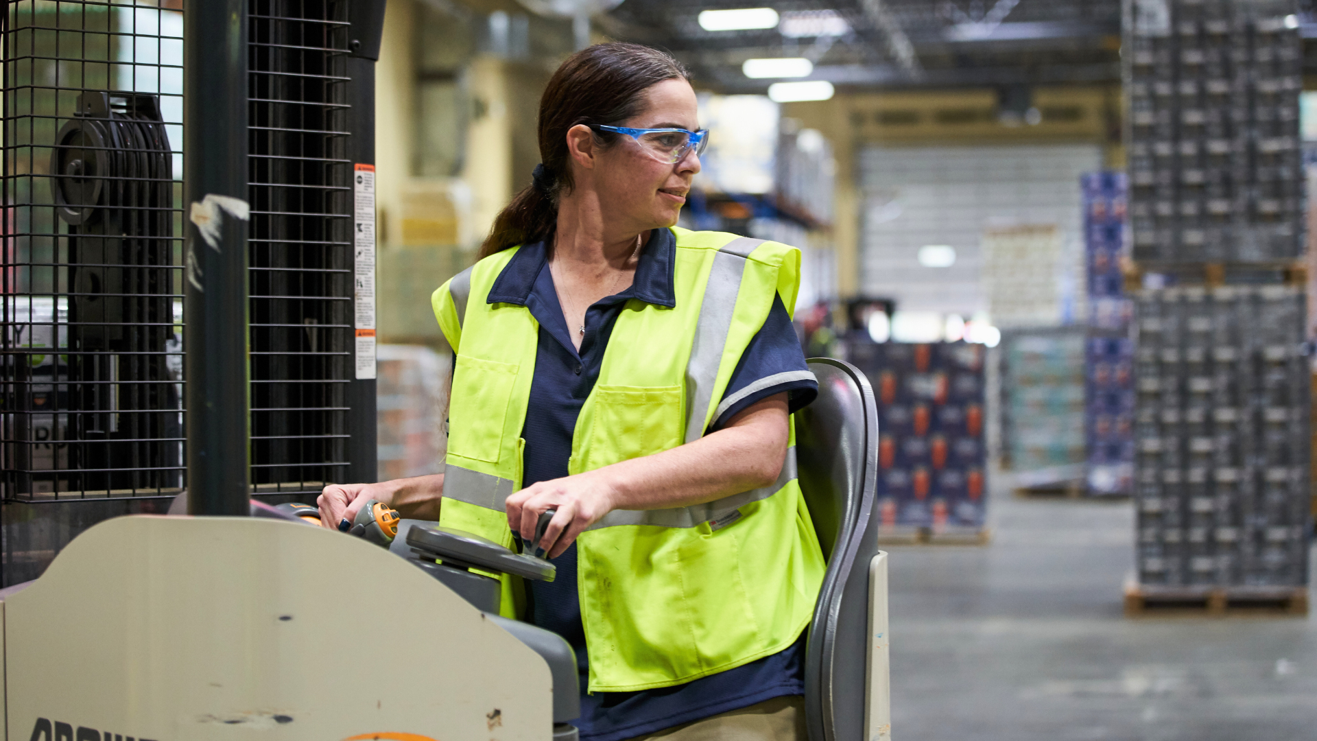 Woman wearing safety vest and safety goggles while operating a forklift in a warehouse