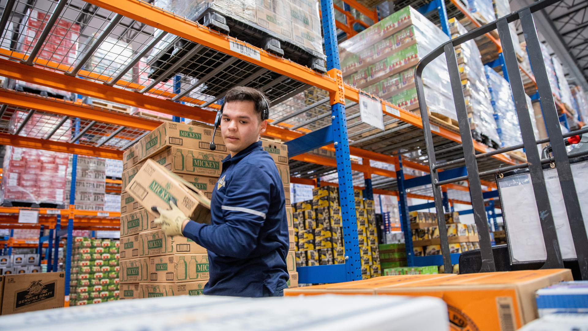 Man in uniform moving a box of product on to a pallet in a warehouse