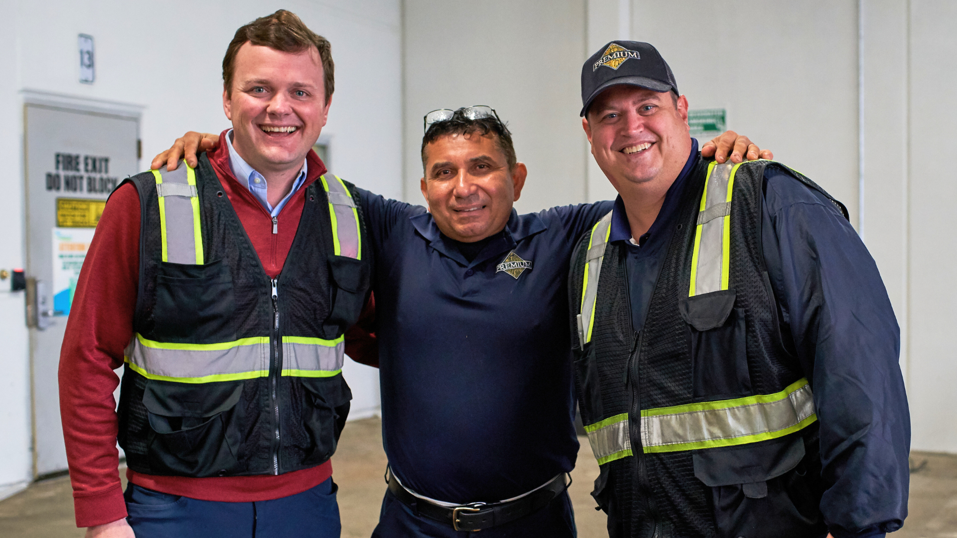 Three people in safety vests smiling in a warehouse