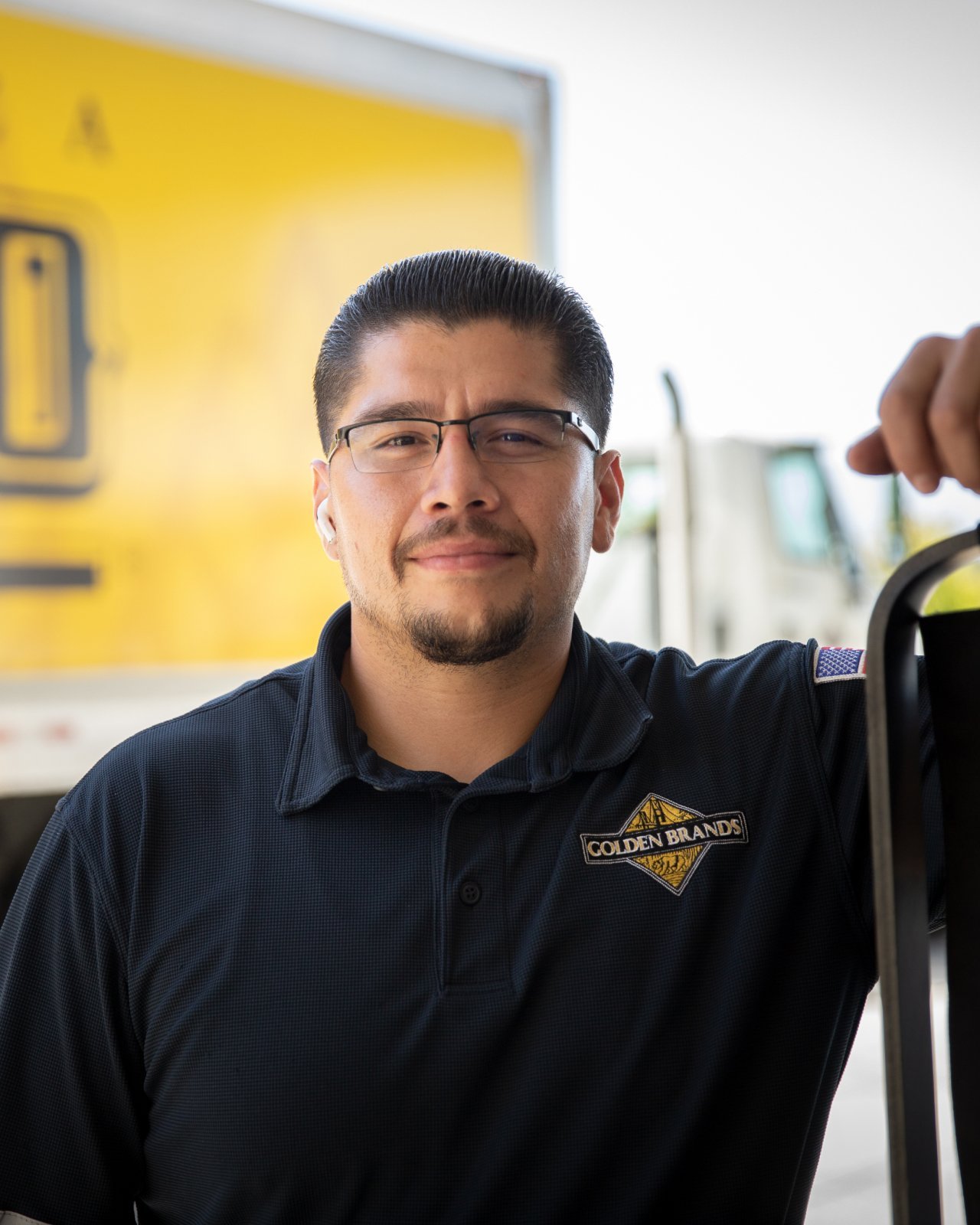 A man wearing a navy polo type shirt standing outside near a yellow truck