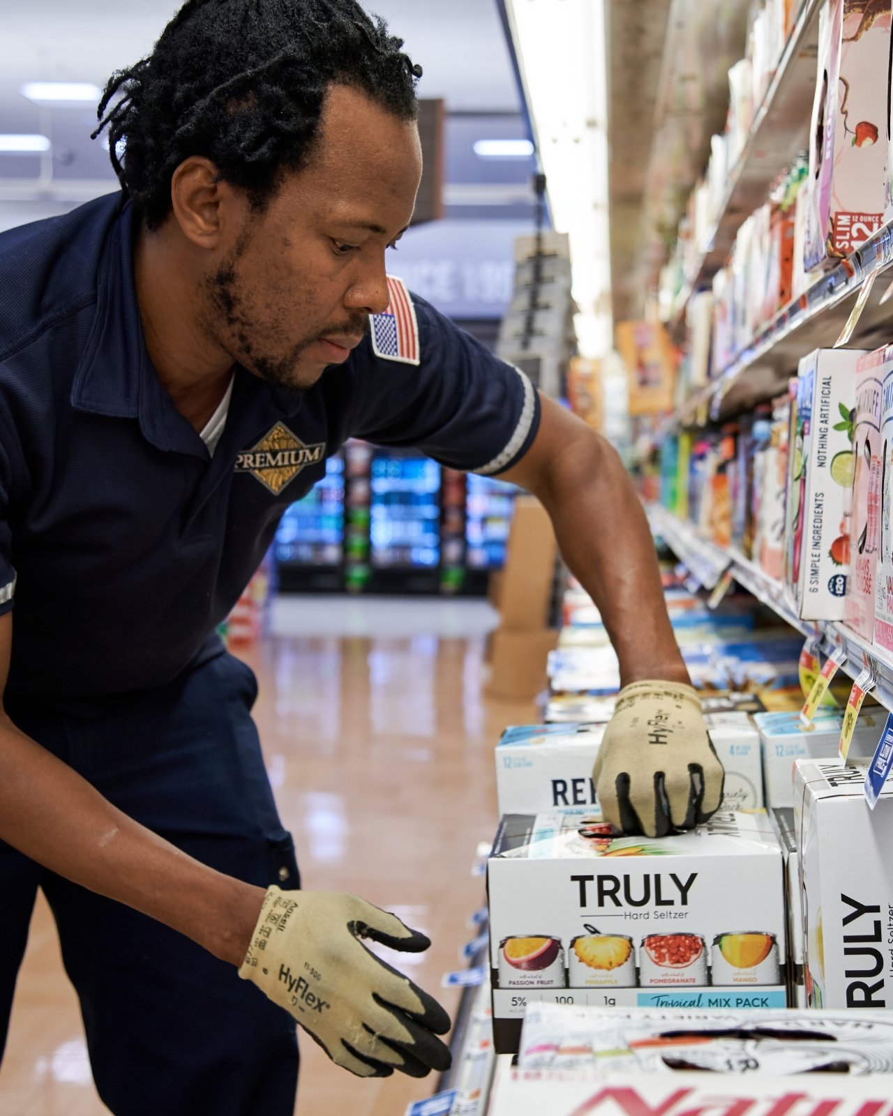A man in a navy polo type shirt adding product to a retail cooler space