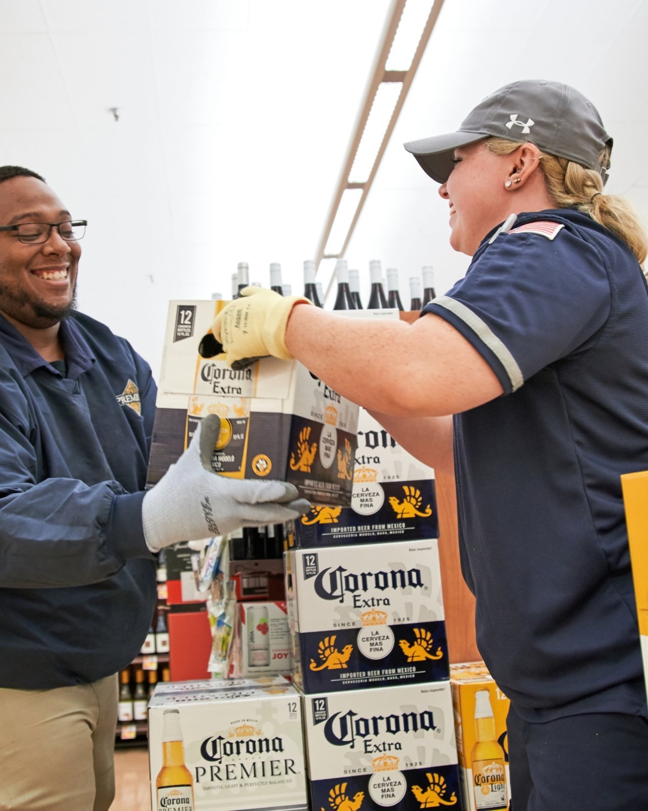 A man and a woman working together in a store aisle putting away a 12-pack of Corona Extra