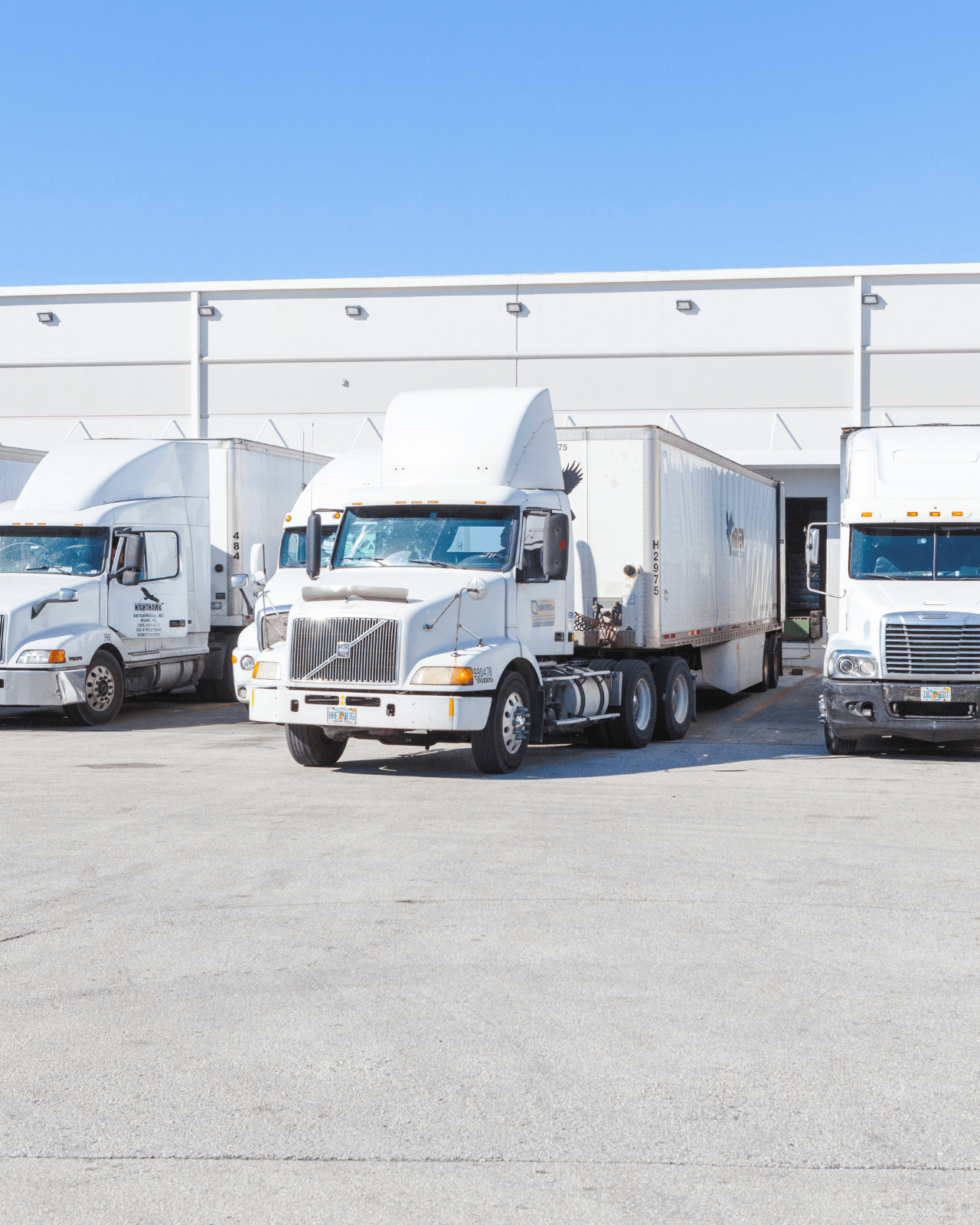 Photo of three delivery trucks parked outside of a warehouse