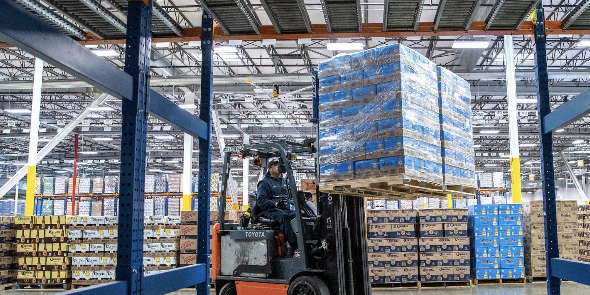 A wide view of man on a forklift with two pallets full of Modelo Especial in a warehouse near a racking system