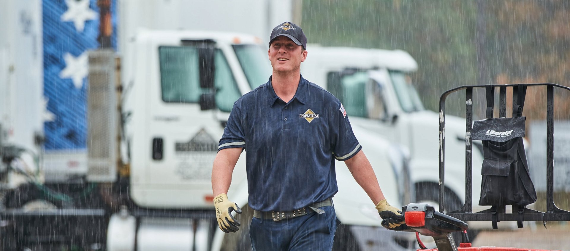 A man wearing a navy hat and polo shirt smiling while walking outside in the rain